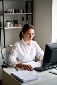 Nail salon manager analyzing employment records and tax documents on a computer, illustrating worker classification in the beauty industry.